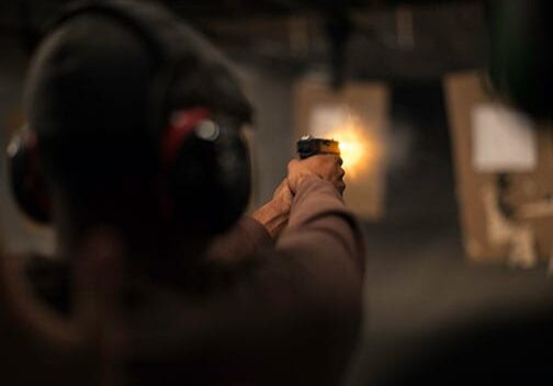 Person firing handgun at shooting range target.